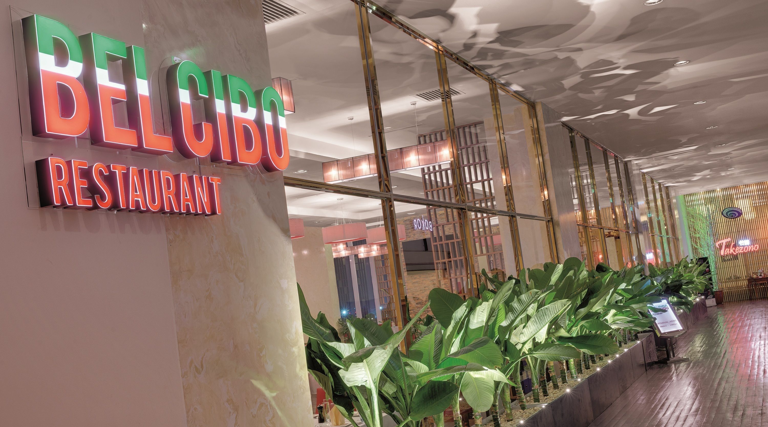 A modern interior with a 'BELCIDO RESTAURANT' sign, a glass partition, and indoor plants.