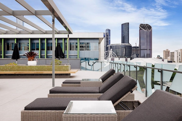 Un bar en la azotea con mesas al aire libre, vistas del horizonte urbano y edificios modernos al fondo.