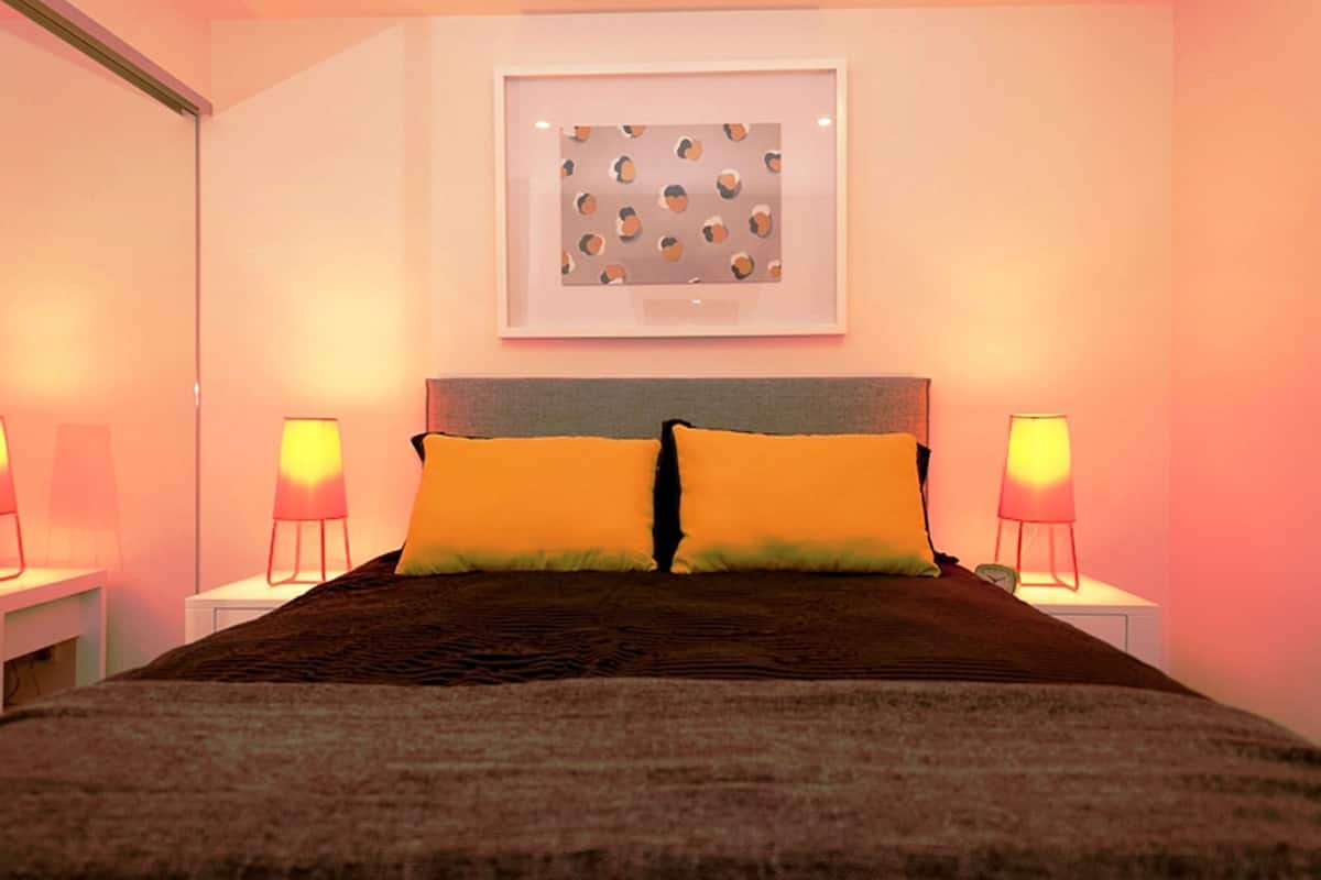 Un dormitorio con una cama, dos lámparas de noche, un cuadro en la pared y una mesita de noche.