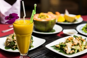 A dining table with a glass of orange juice, a plate of food, and a bowl of fruit. - Robam Inn (Siem Reap)