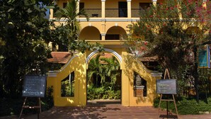 A yellow building with arched windows and a central archway. There are signs on either side of the archway listing spa treatments. - Robam Inn (Siem Reap)