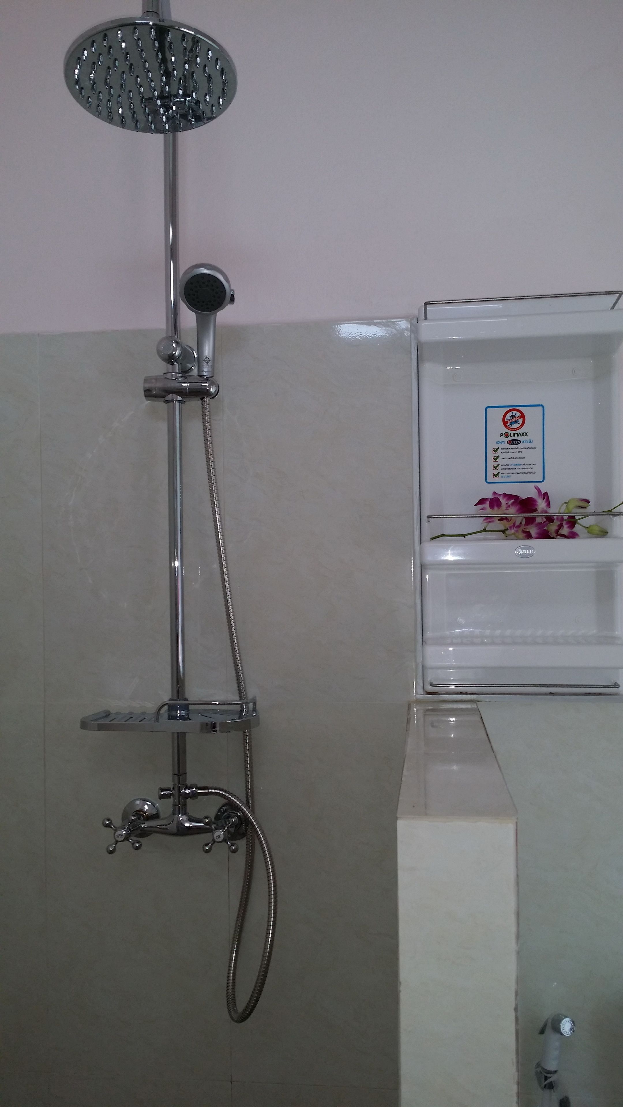 Een douche met een handdouche en een stortdouche, een handdoekhouder en een bordje met een rookverbodssymbool.