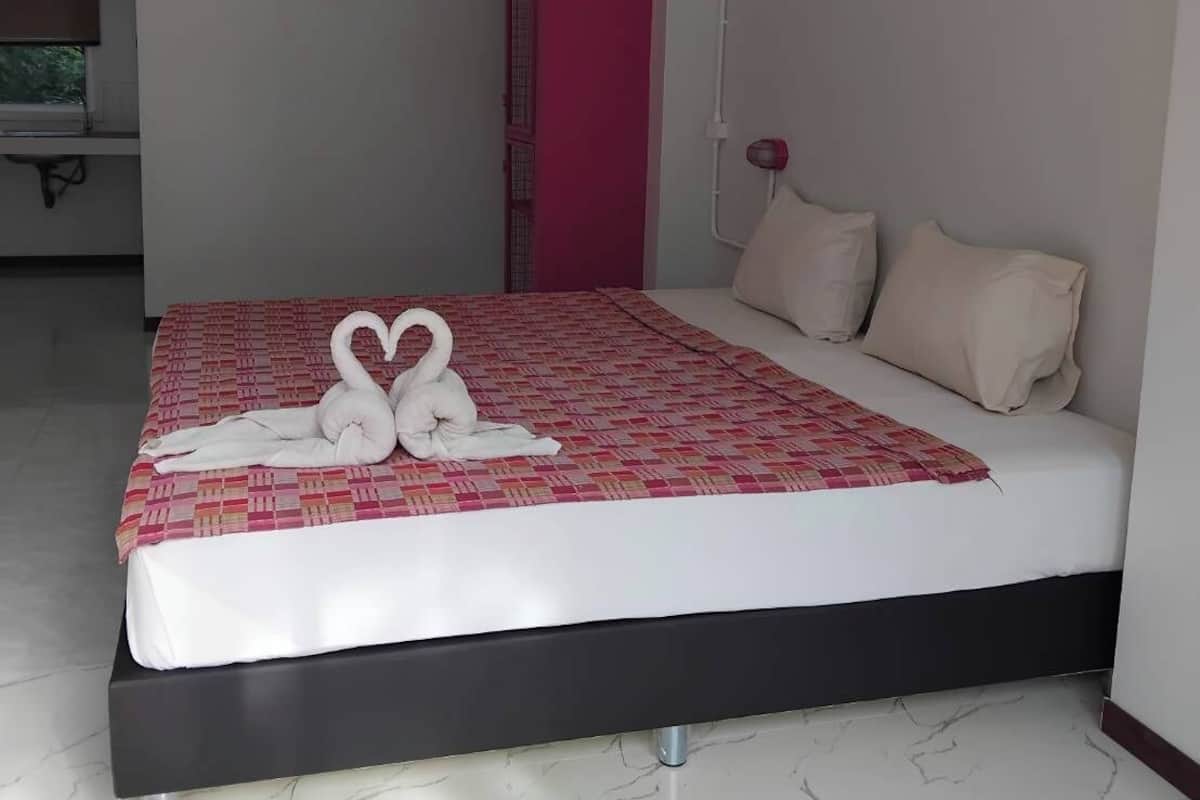 Habitación de hotel con una cama, un armario rojo, un televisor y aire acondicionado instalado en la pared.