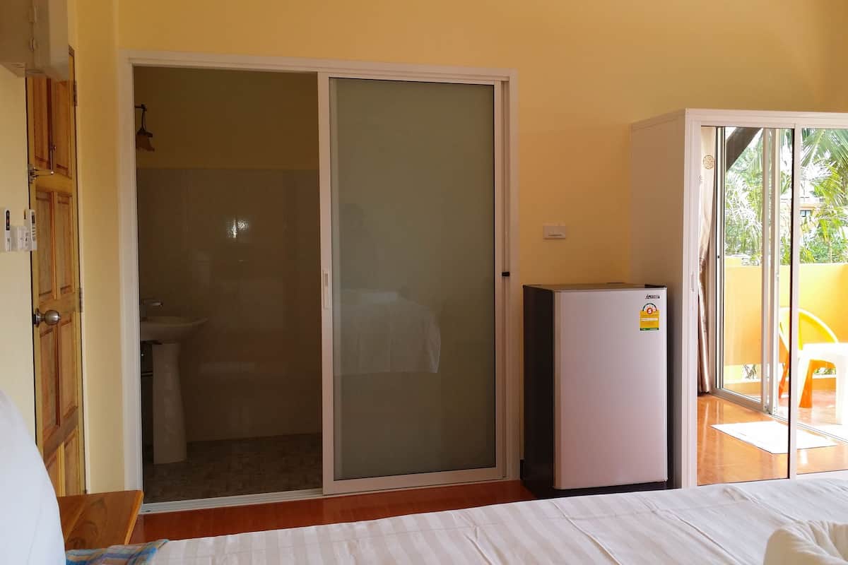 Una habitación con una cama, puerta corrediza de vidrio a un balcón, un refrigerador pequeño y un baño con inodoro y lavamanos.