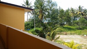 Een balkon met een gele muur en uitzicht op een weelderig groen landschap met palmbomen.