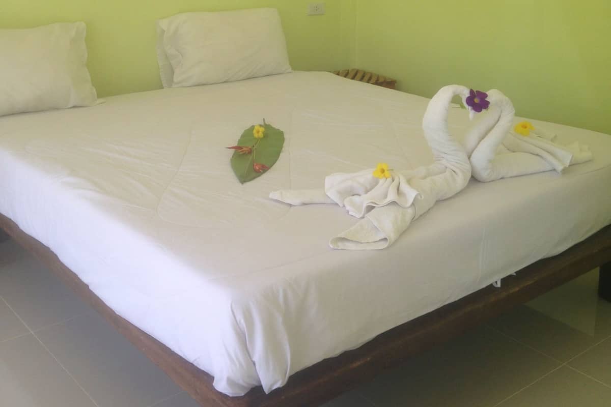 Una cama con sábanas blancas, pared verde y cabecera de madera.