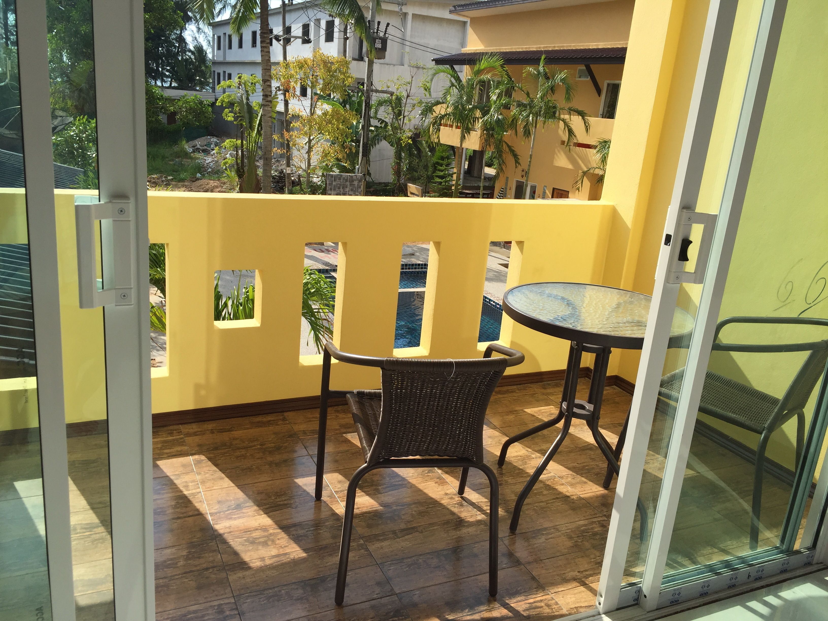 Ein Balkon mit Tisch und Stühlen, einer Glastür und Blick auf einen Pool und Gebäude.