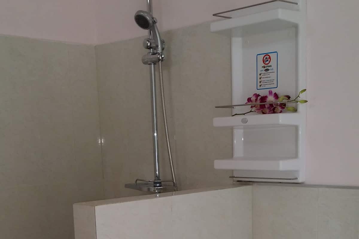 Un baño con ducha, inodoro y un pequeño estante con flores.