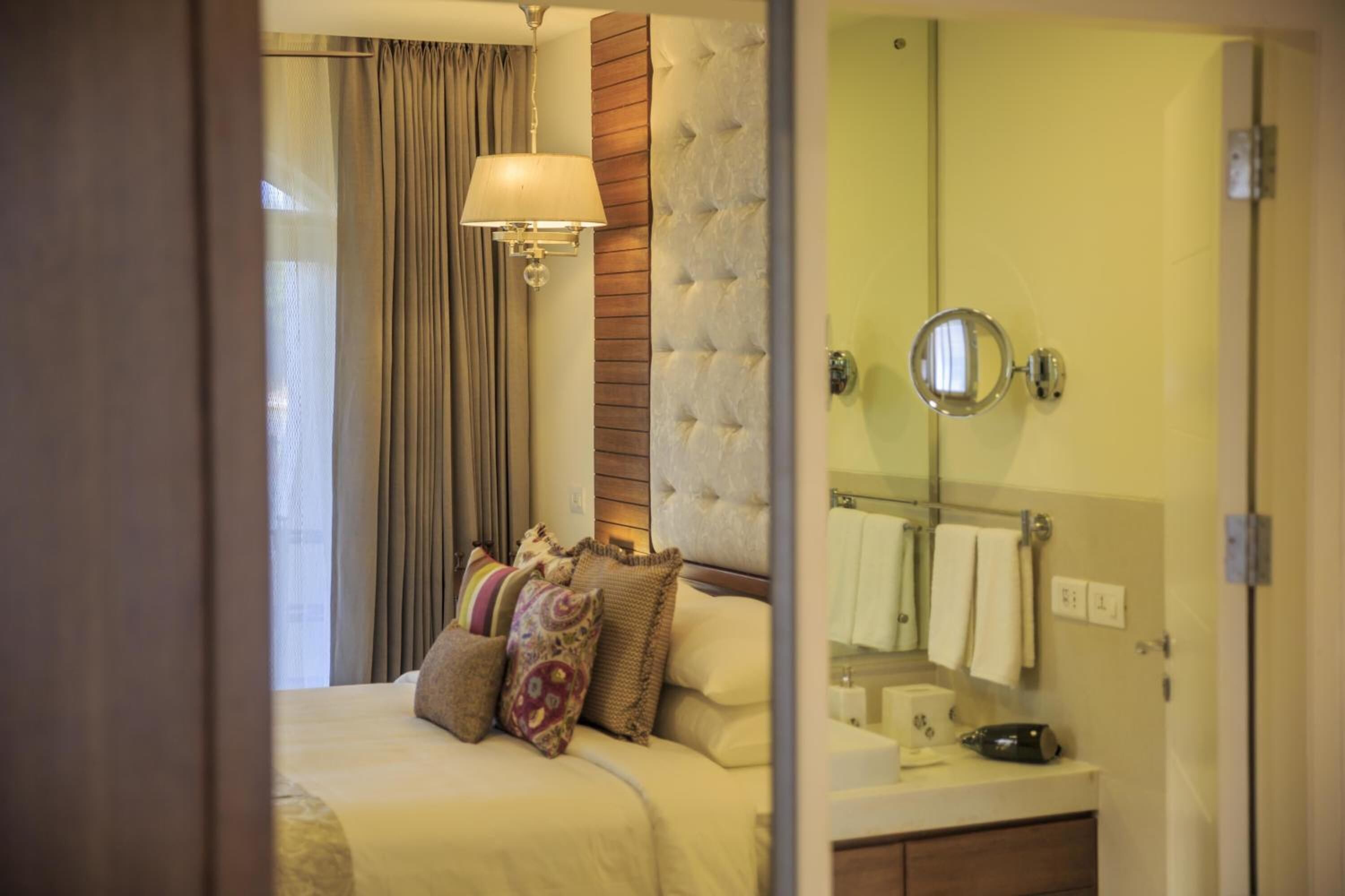 A hotel room with a bed, a bedside lamp, a mirror, and a bathroom with a towel rack.