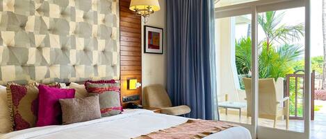 A hotel room with a large bed, a wooden headboard, a ceiling fan, a view of the outdoors, and a balcony with chairs.
