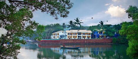 A waterfront hotel with a stone wall, a boat, and palm trees.