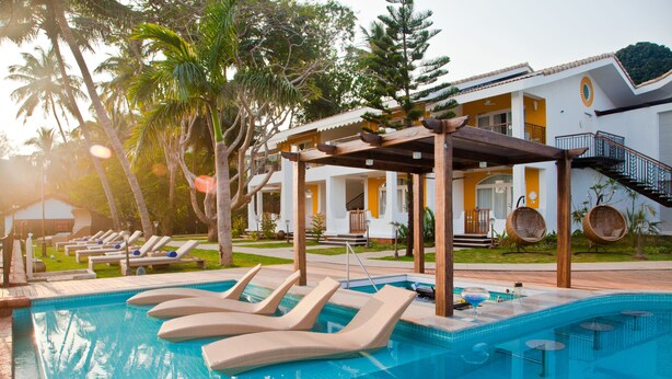 A pool area with lounge chairs, a pergola, and a building with a staircase.