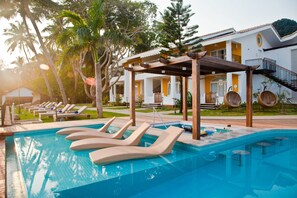 A pool area with lounge chairs, a pergola, and a building with a staircase. - Acron Waterfront Resort (Baga)