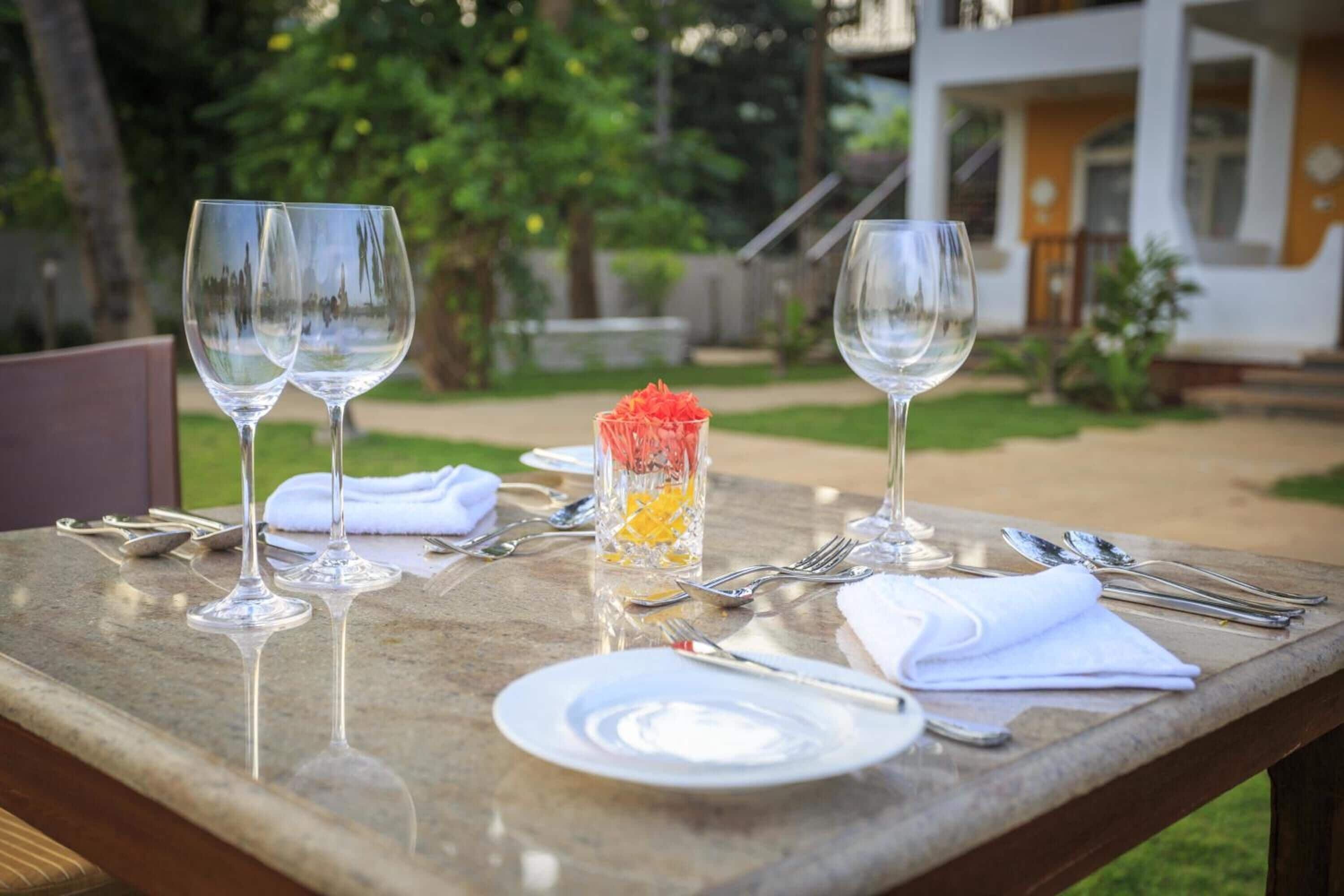 Une table dressée à l’extérieur, avec deux verres à vin, un verre de jus d’orange et des couverts.