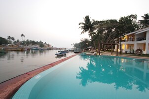 En swimmingpool med tilknyttede både, en terrasse med palmer og en bygning med altaner.