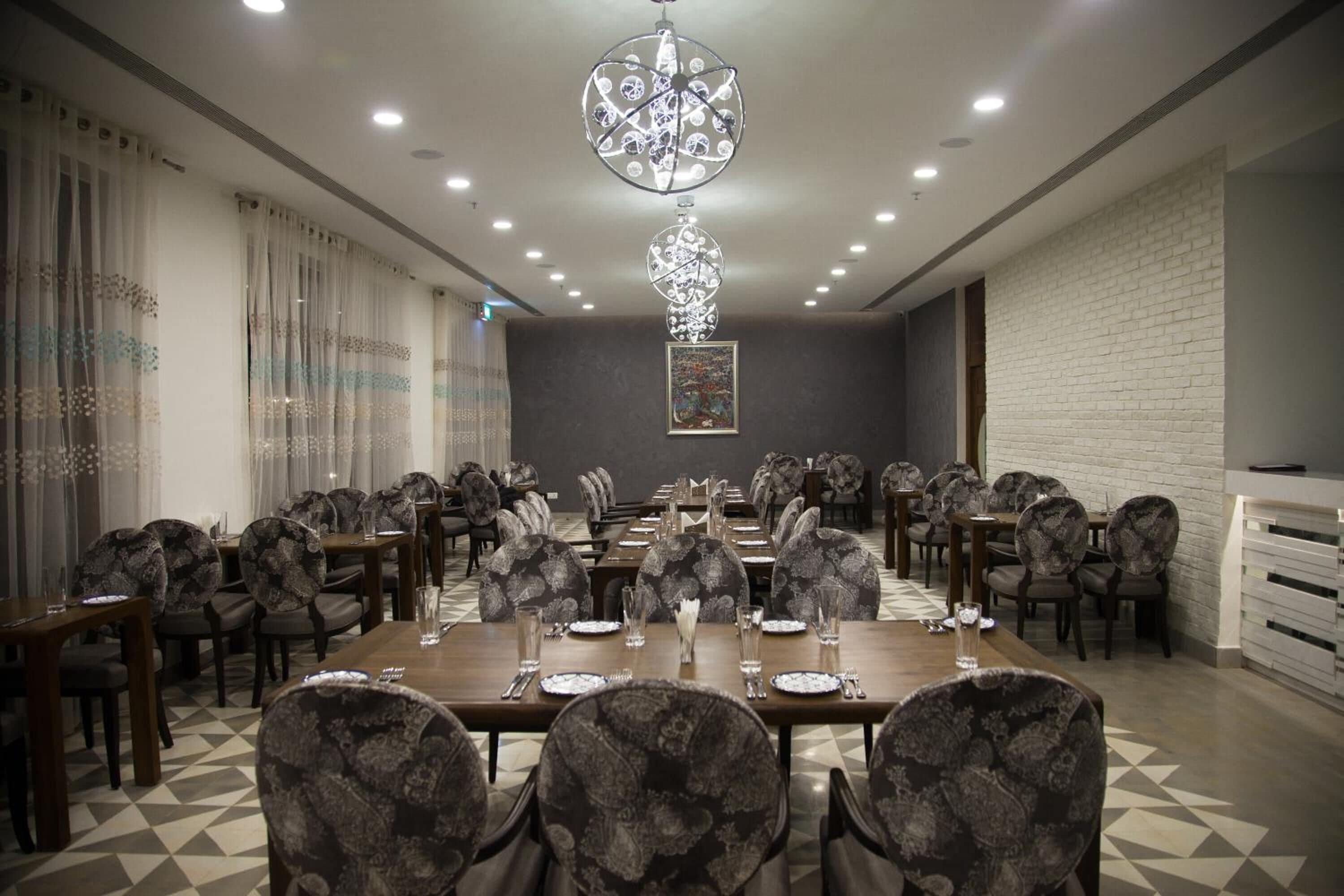 A conference room with a long table, patterned chairs, a chandelier, and a white brick wall.