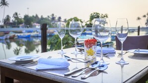 A table set for dining with clear glassware and a decorative glass centerpiece, overlooking a body of water with boats.