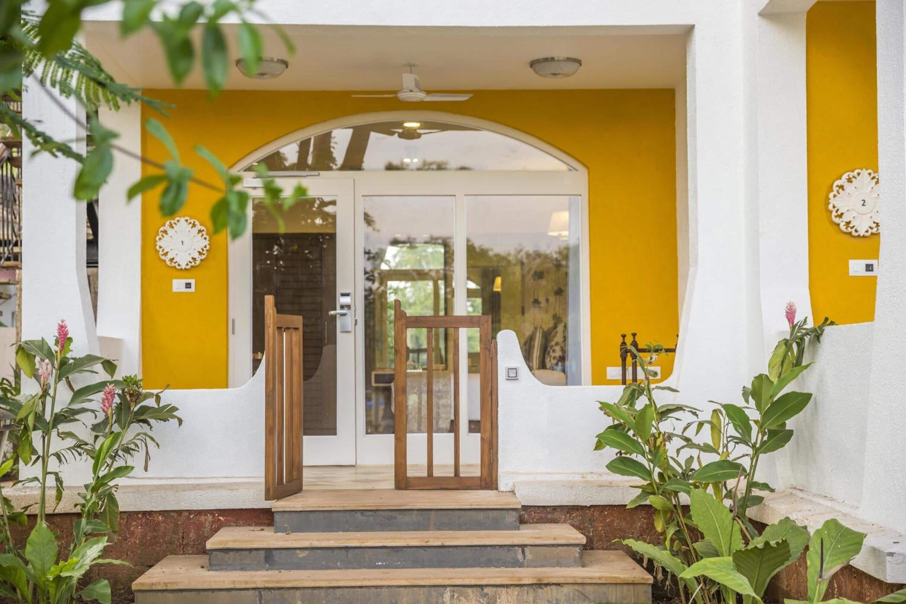 A yellow and white building with a wooden door, steps, and a ceiling fan.