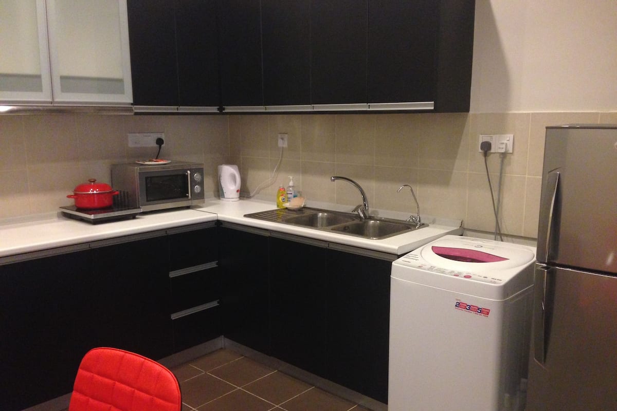 Una cocina compacta con microondas, tostadora, lavamanos y un refrigerador pequeño.