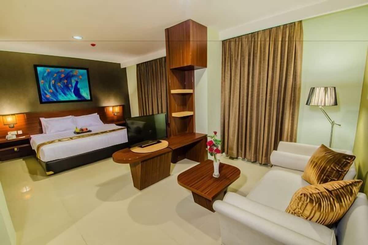 A hotel room with a bed, a sofa, a TV, a desk, and a large window with curtains.