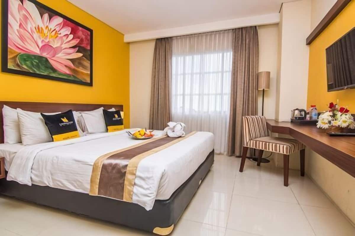 A hotel room with a bed, a desk, a chair, a painting, and a window with curtains.