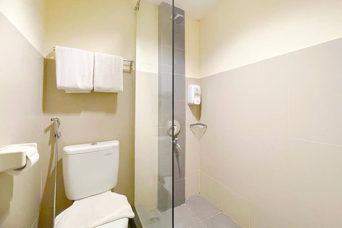 A bathroom with a toilet, a glass shower enclosure, a towel rack with two towels, and a soap dispenser.