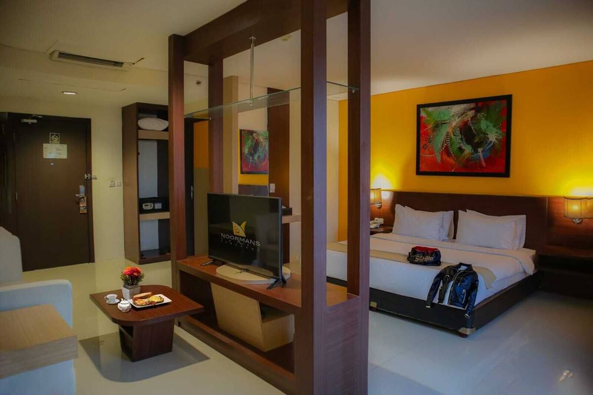 A hotel room with a bed, a TV, a desk with a coffee cup, and a painting on the wall.