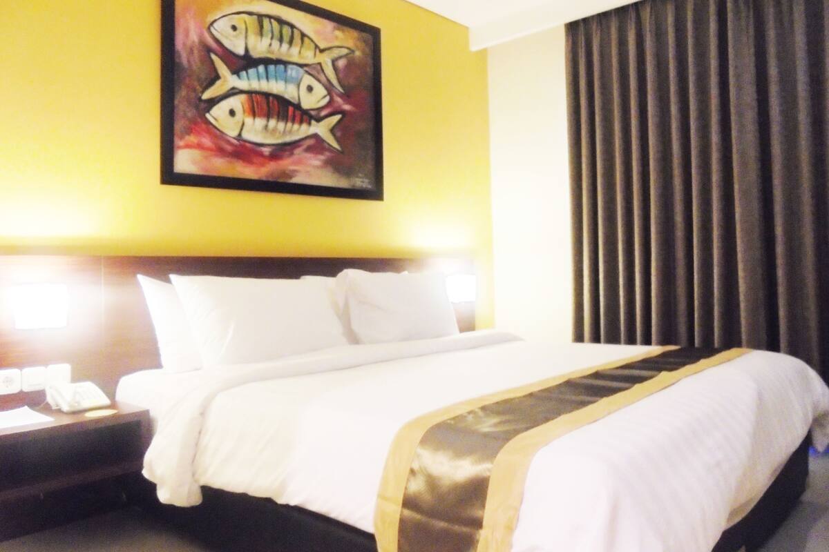 A hotel room with a bed, a nightstand, a painting, and a curtain.