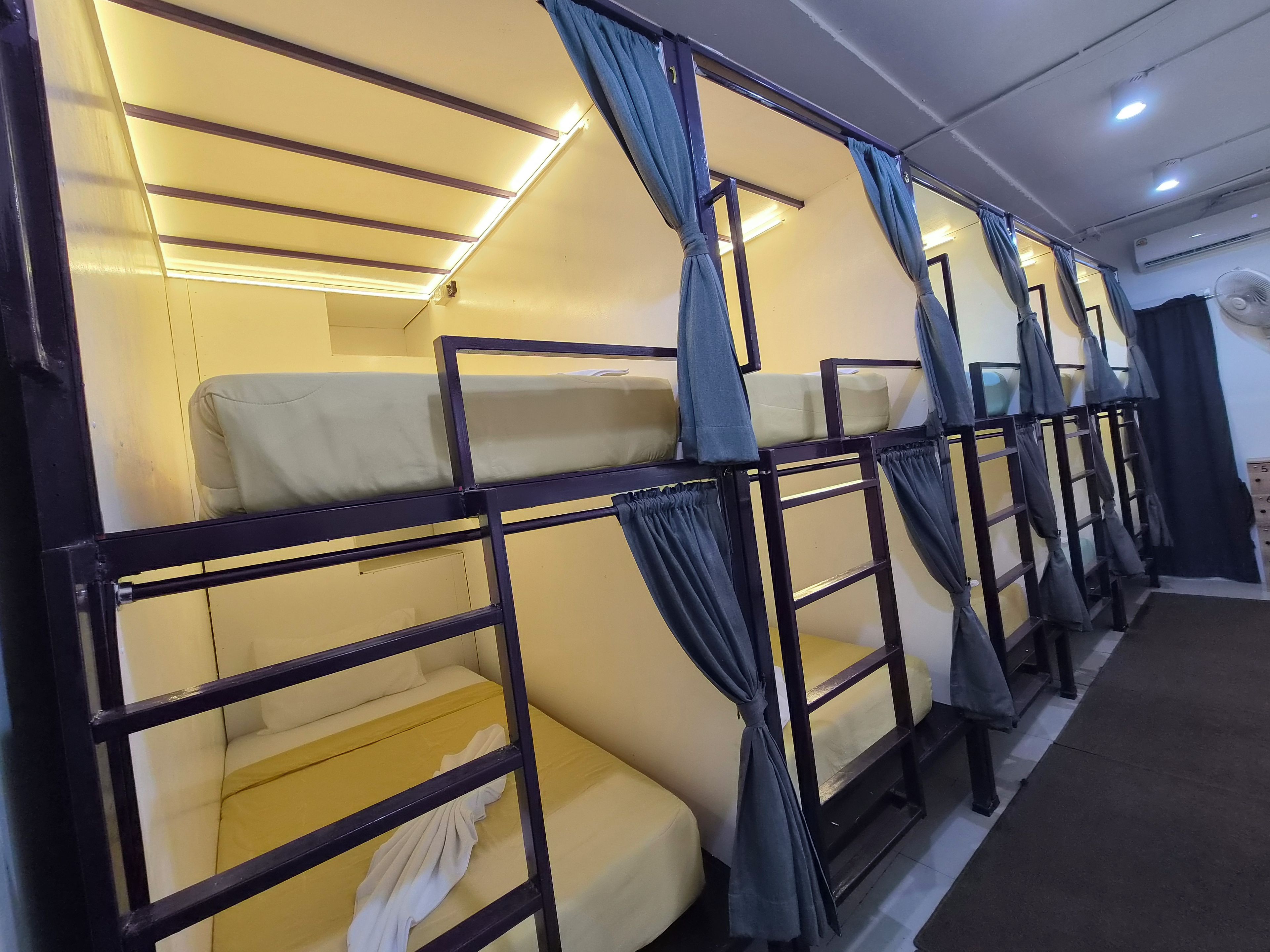 A row of bunk beds with curtains, a ceiling fan, and a visible air conditioning unit.