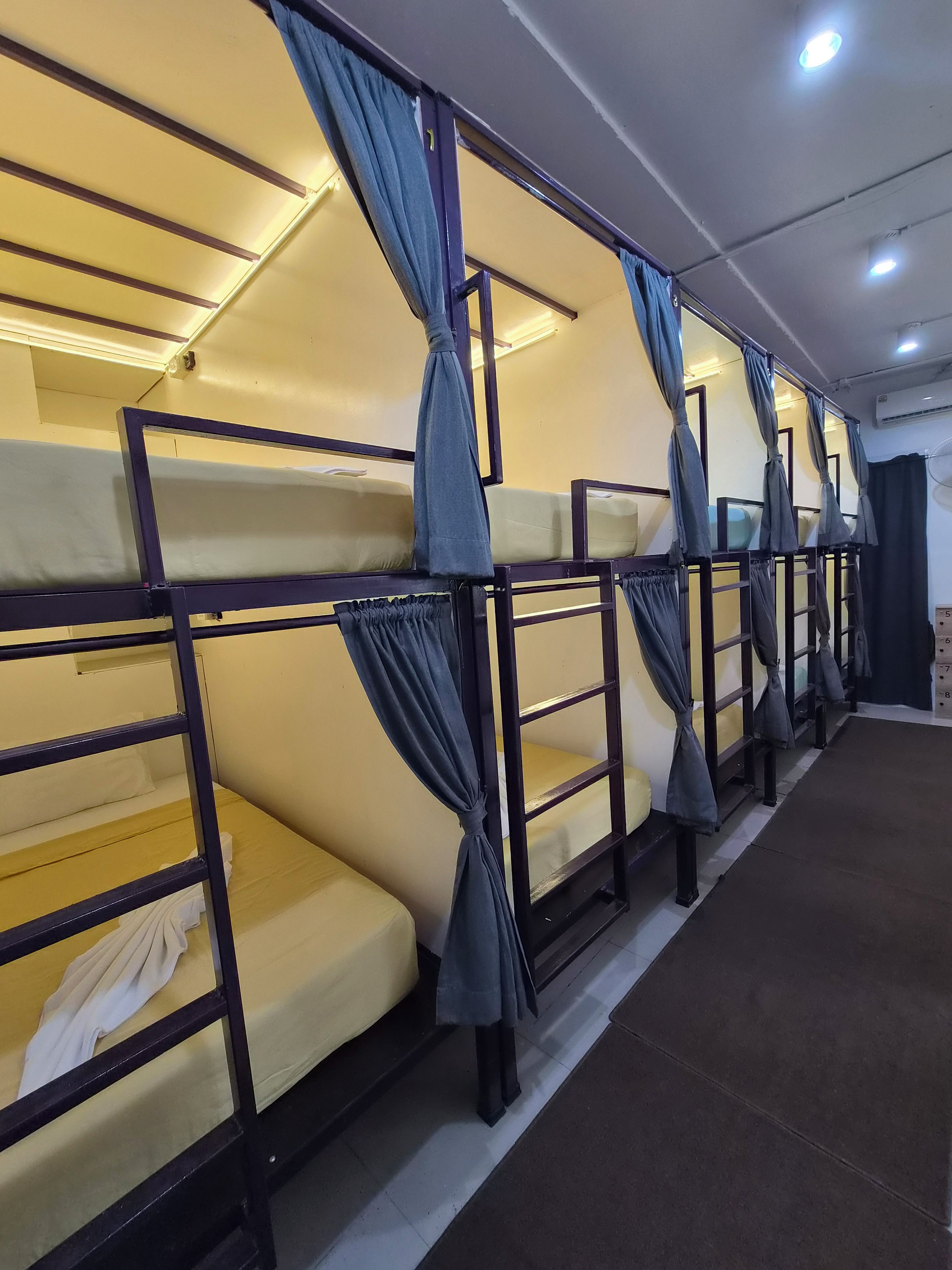 A row of bunk beds with curtains, a tiled floor, and an air conditioning unit on the wall.