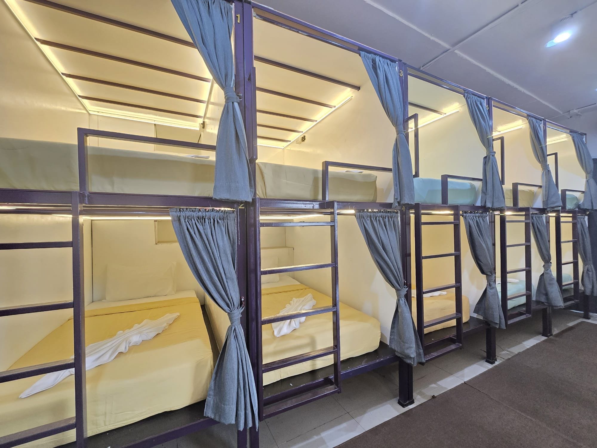A row of bunk beds with curtains, each bed has a mattress and a pillow.