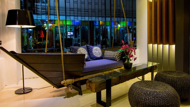A modern interior with a hanging swing, a glass coffee table, and a sofa with patterned cushions. - Hotel The Journey Patong New (Patong)