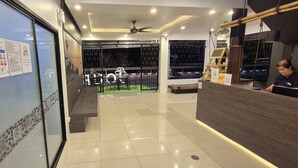 A hotel reception area with a reception desk, a seating area with chairs, and a glass wall displaying safety guidelines. - Hotel The Journey Patong New (Patong)
