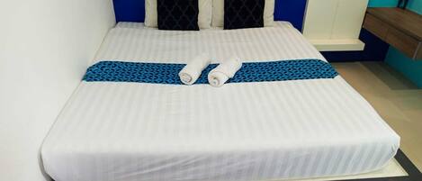 Una cama bien hecha con una colcha blanca a rayas, dos almohadas negras con un diseño geométrico y un corredor de cama azul y negro estampado.