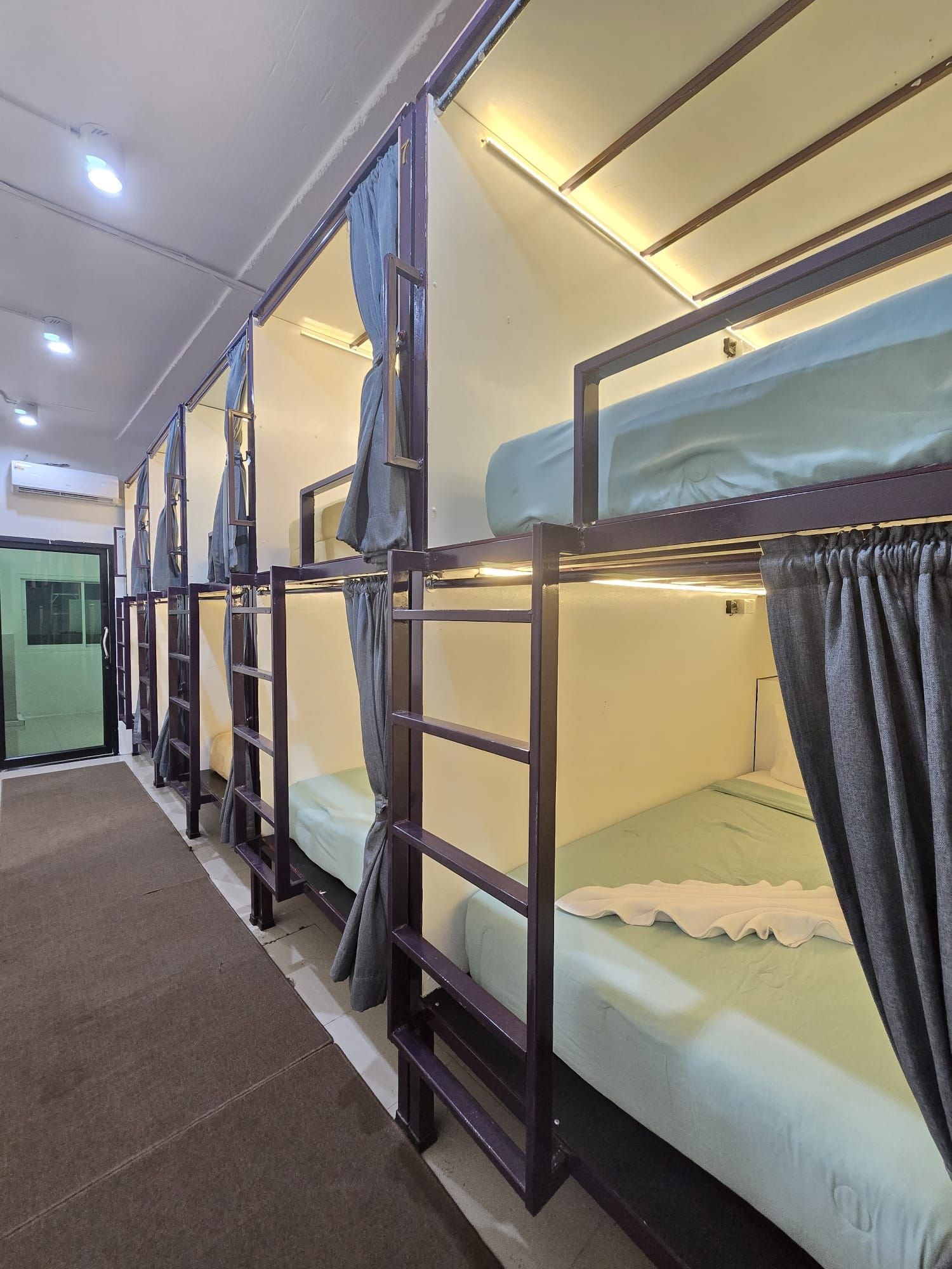 A row of bunk beds with curtains, a green door, and a white wall.