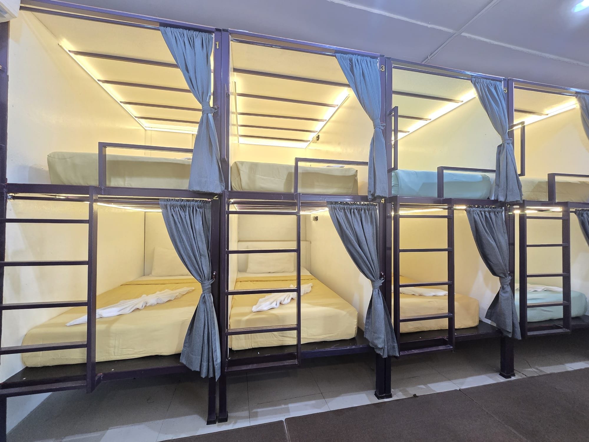 A row of bunk beds with curtains, each bed has a mattress and pillows.