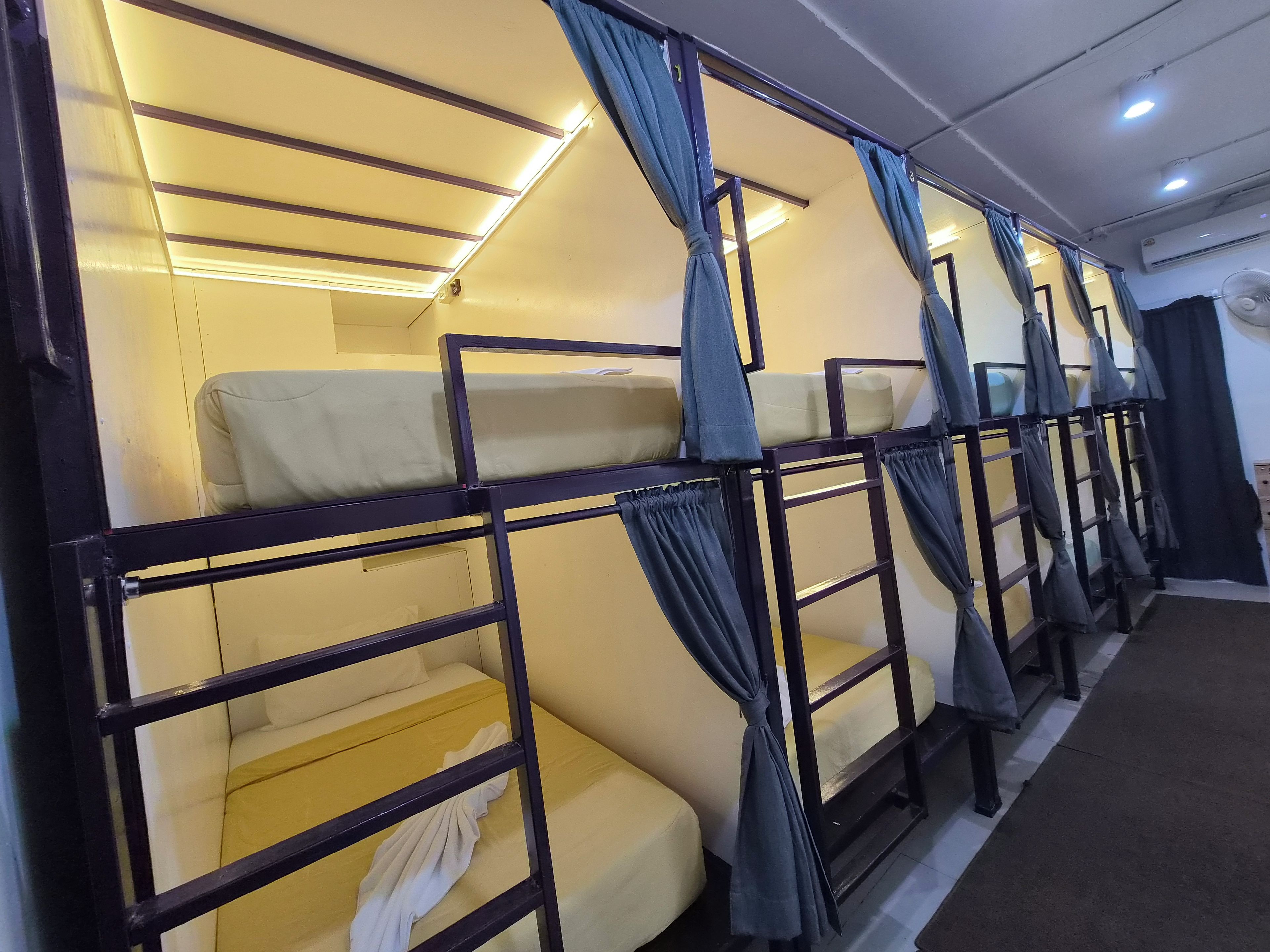 A row of bunk beds with curtains, a ceiling fan, and a window with curtains.