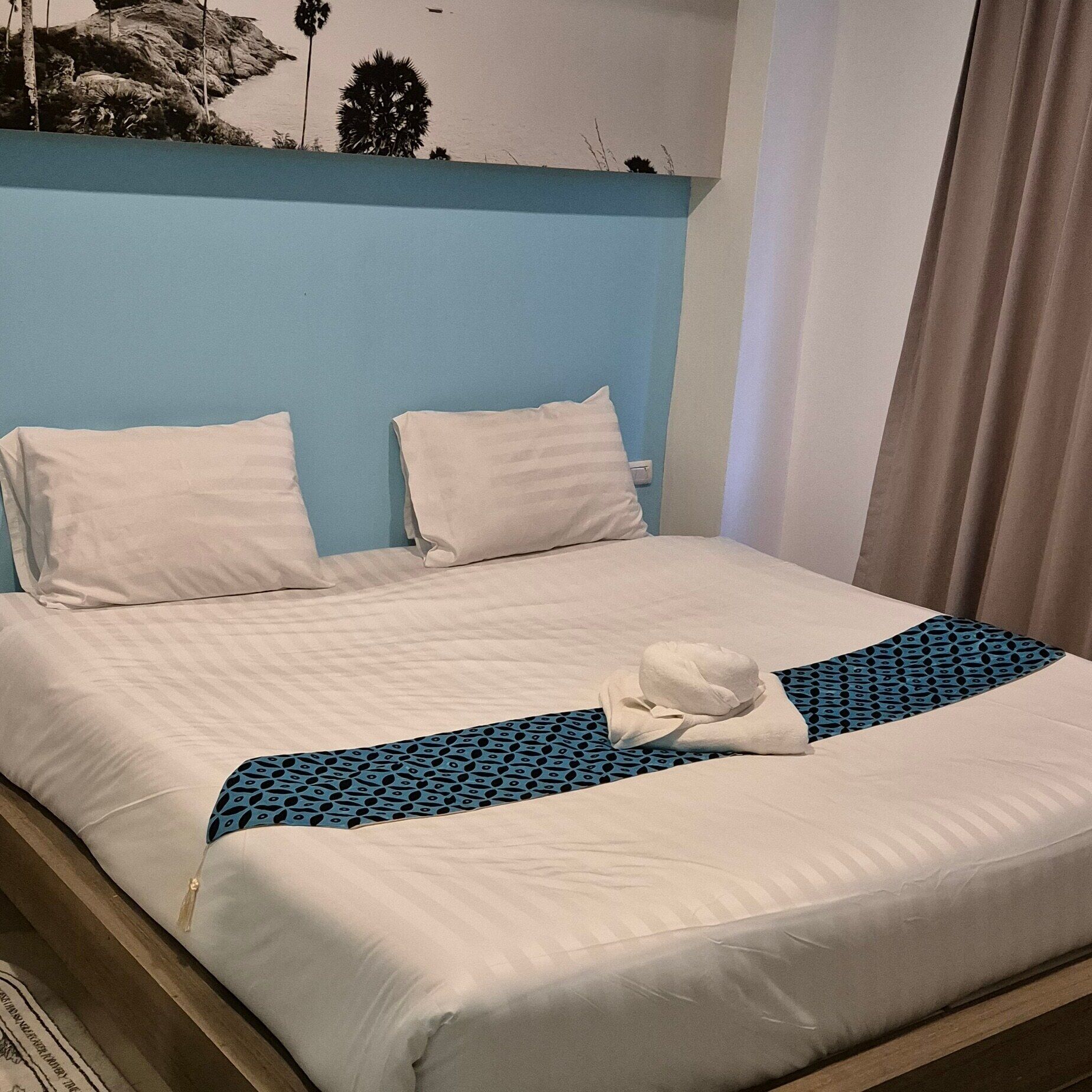 A neatly made bed with white linens, a blue patterned throw, and a white towel folded on the bed.
