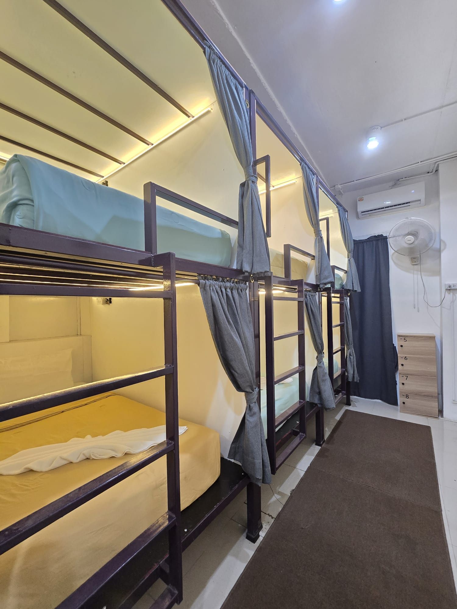 A bunk bed room with a ceiling fan, an air conditioning unit, and a wooden dresser with drawers.