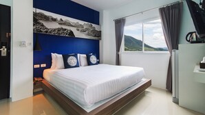 A modern hotel room with a large bed, a mounted television, and a scenic view of mountains through the window. - Hotel The Journey Patong New (Patong)