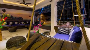 A modern lounge area with a swing chair, cushioned seating, and a ceiling fan. - Hotel The Journey Patong New (Patong)