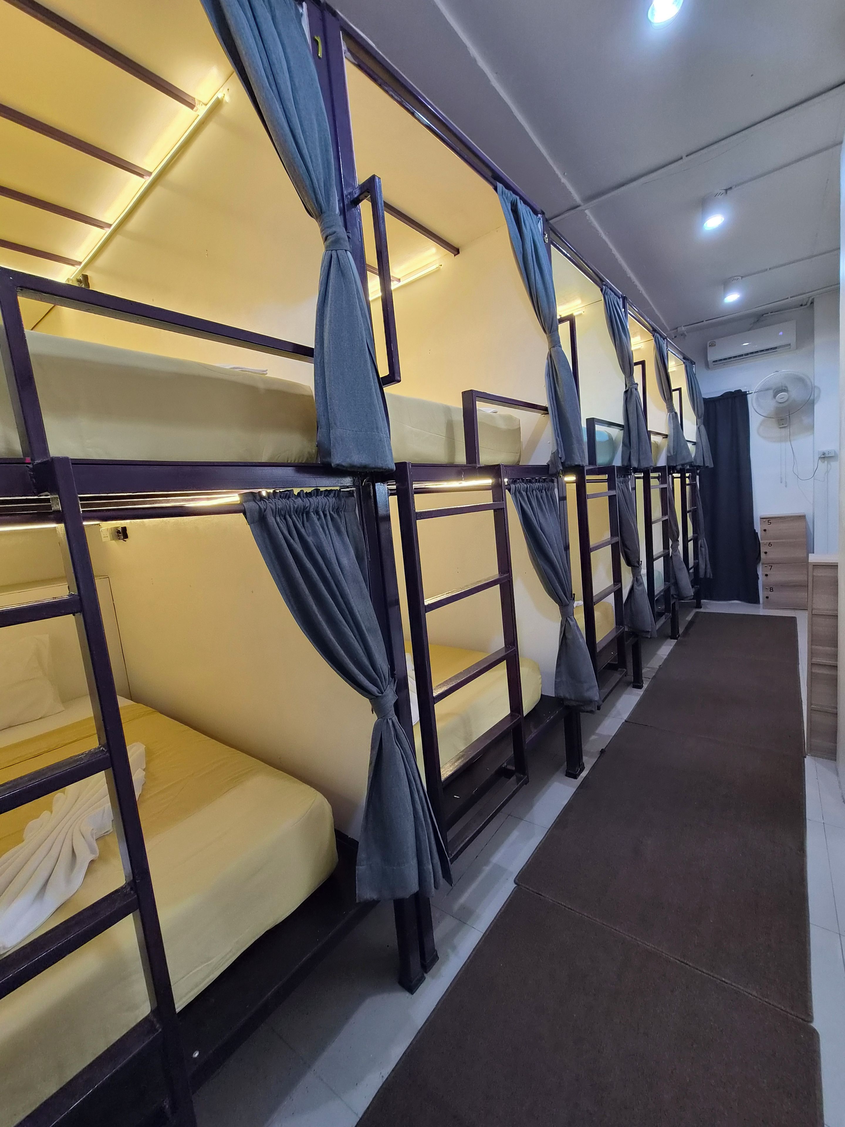 A row of bunk beds with curtains, a fan, and a wooden dresser with drawers.