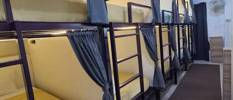 A row of bunk beds with curtains, a fan, and a wooden dresser with drawers.
