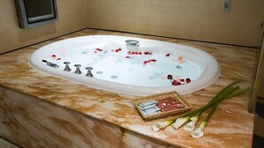 A spa bath with rose petals, a tray of toiletries, and a mirror on a marble floor. - Crystal Motel (Hsinchu)