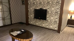 A hotel room with a television mounted on a wall decorated with logs, a small round table with a remote control, and a trash bin. - Crystal Motel (Hsinchu)