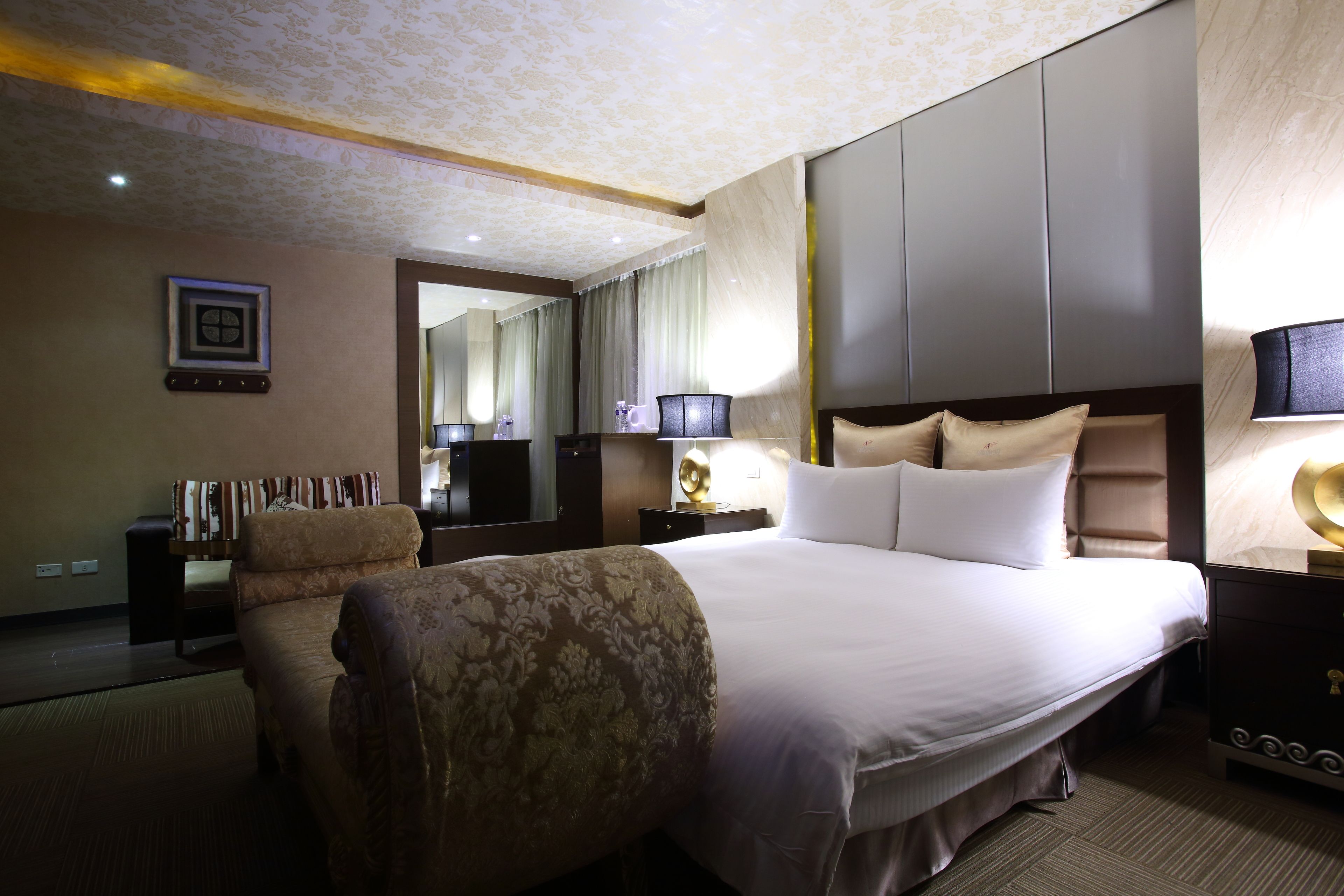 A hotel room with a large bed, a sofa, a desk, and a mirror.