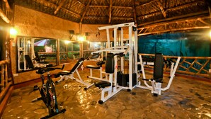 Une salle de sport intérieure équipée de matériel d’exercice, dotée d’un sol en pierre et d’un toit de chaume.