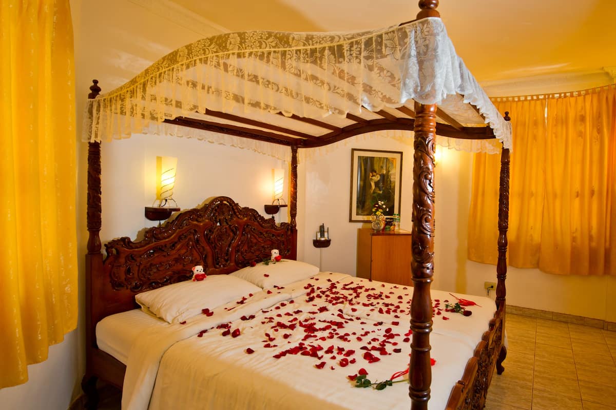 Ein Bett mit Baldachin, auf dem Rosenblätter auf der Bettdecke verteilt liegen, ein Holzkopfende und ein Baldachin.