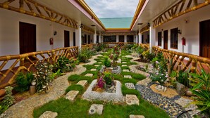 Une cour intérieure avec un jardin central, des garde-corps en bambou et un toit en tuiles.