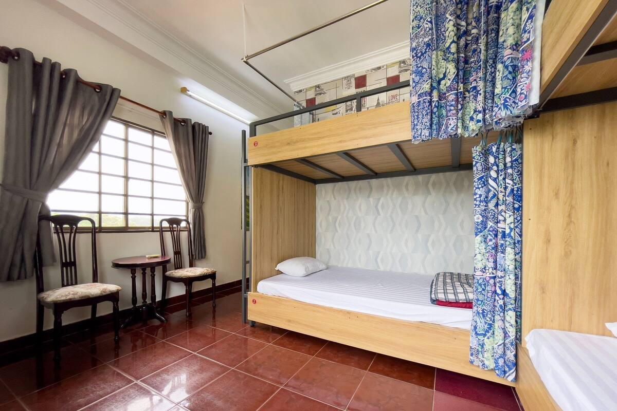 Une chambre avec un lit superposé, une fenêtre, des chaises et une table.